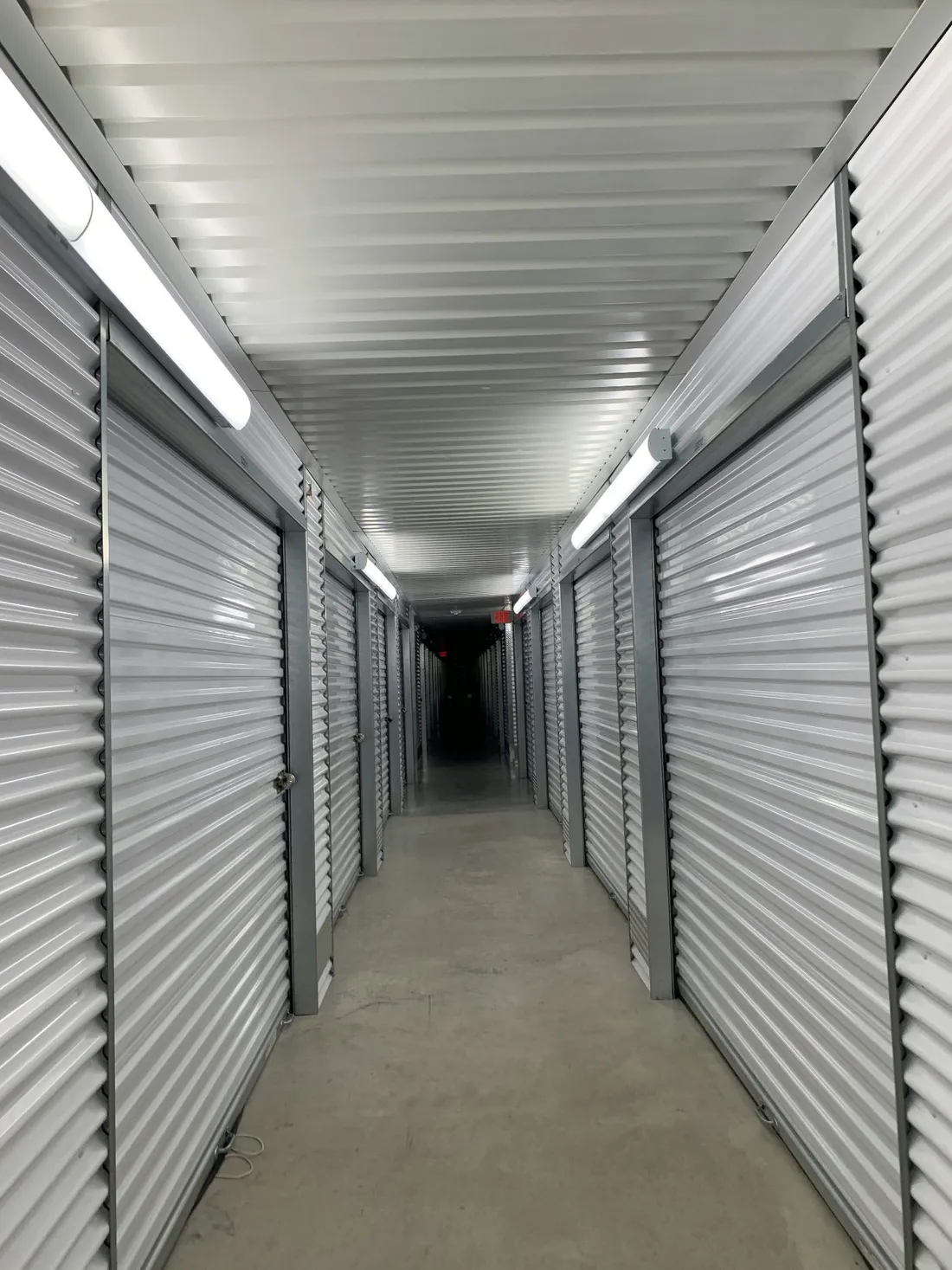 White-walled interior storage corridor with bright overhead lighting and roll-up doors
